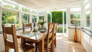 A conservatory with a wooden table, chairs, and a vase of flowers. - Charming Countryside Cottage (Blandford Forum)
