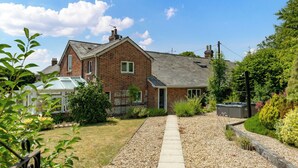 A brick house with a sloped roof, a front porch, and a gravel driveway leading to the entrance. - Charming Countryside Cottage (Blandford Forum)