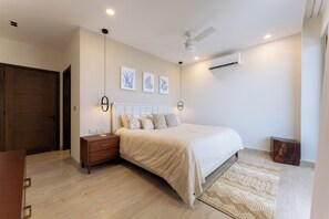 Ein Schlafzimmer mit Bett, Nachttisch, Wand-Klimaanlage, Deckenventilator und Kunstwerk.