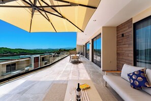 A modern outdoor balcony with a view of the landscape, a seating area with a table, and a sofa. - Main Level 3BR | Oceanview & Private Pool (Huatulco)