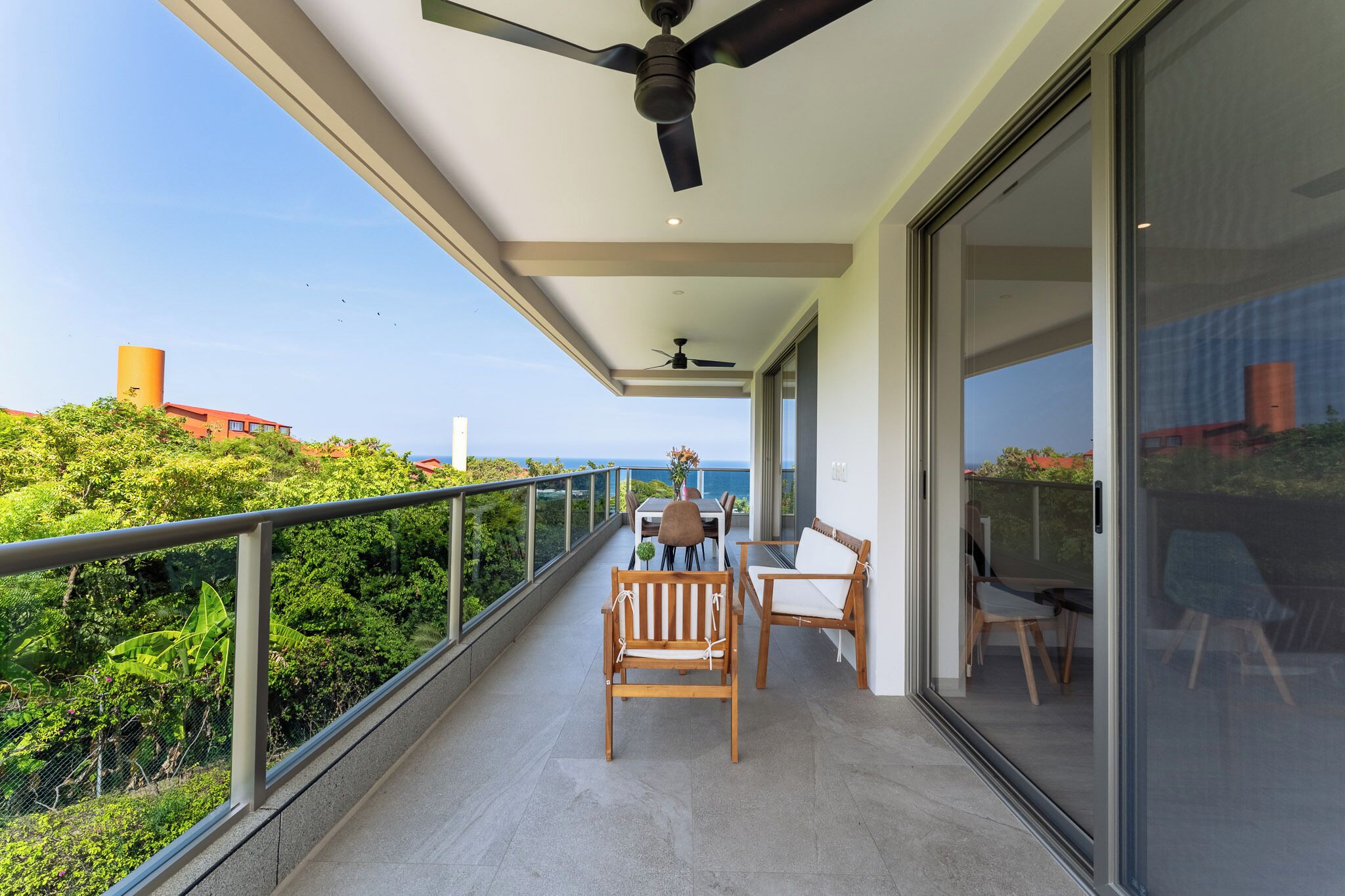 Un balcon avec une table et des chaises, un ventilateur de plafond et une vue sur l’océan.