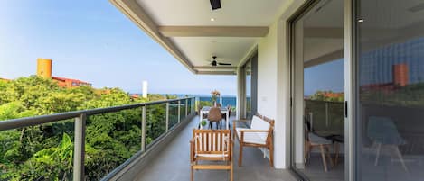 A balcony with a table and chairs, a ceiling fan, and a view of the ocean.