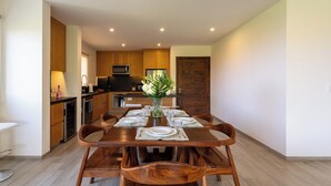 A modern kitchen with wooden cabinets, a dining table set for four, and a vase of flowers. - 2nd Level 2BR | Oceanview & Beach Access (Huatulco)