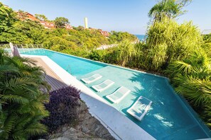 A swimming pool with lounge chairs, surrounded by lush greenery and overlooking a coastal area.