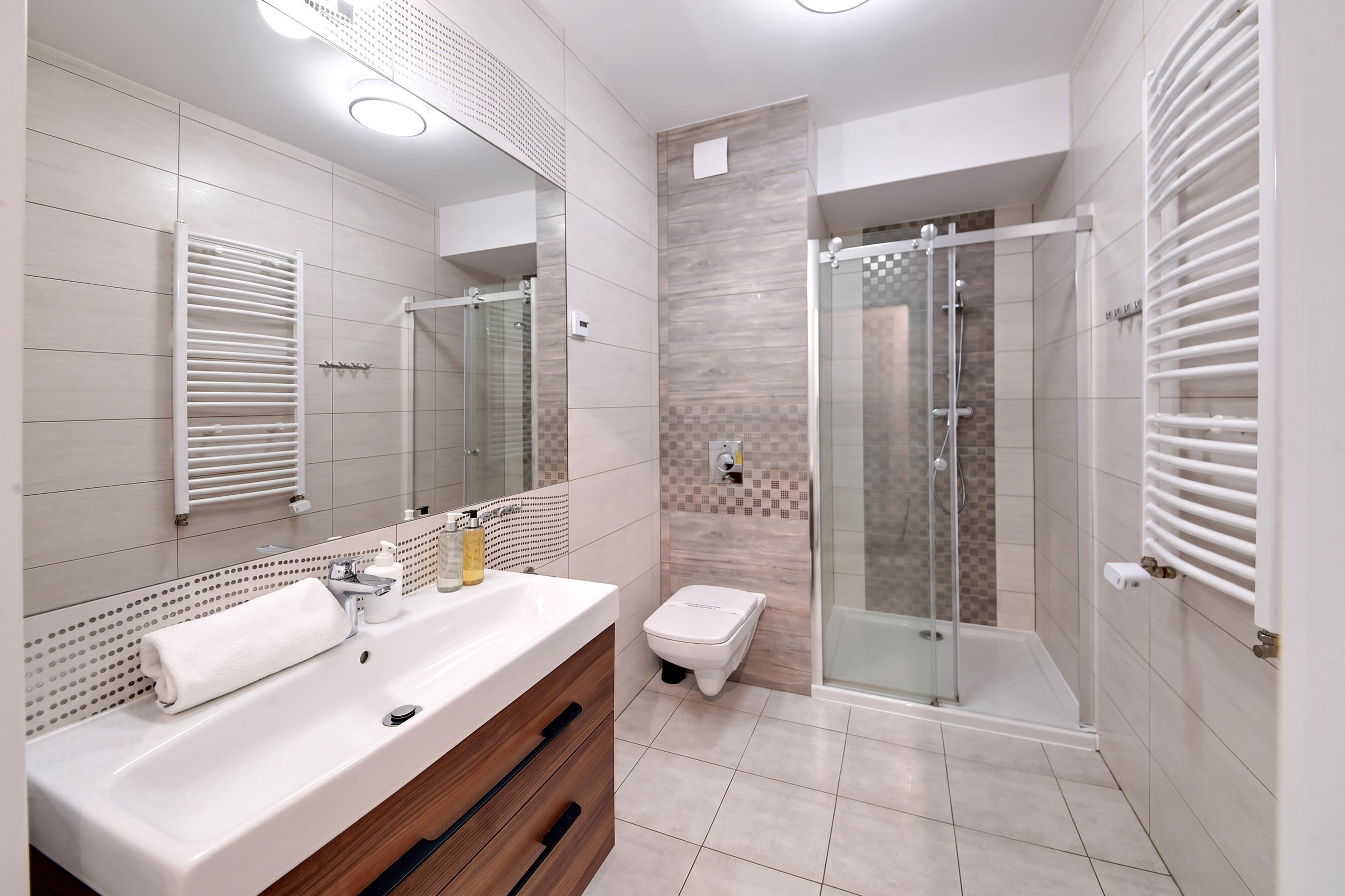 A modern bathroom with a large mirror, a white sink, a glass shower enclosure, and a towel rack.