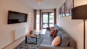Een moderne woonkamer met een flatscreen televisie, een bank met kussens, een salontafel en een kamerkleed met een patroon.