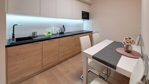 Una cocina moderna con armarios de madera, encimera negra y una zona de comedor con mesa y sillas blancas.