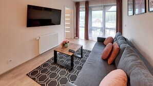 Un salón moderno con un televisor de pantalla plana grande, un sofá con cojines, una mesa de centro con un florero y vistas a través del ventanal.