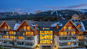 A multi-story hotel with a central entrance and balconies, surrounded by snow-covered mountains. - RentPlanet - Apartament Triventi (Karpacz)