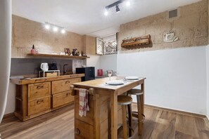 Eine Küche mit Holzschränken, einer Holz-Kochinsel mit Barhocker, einer Kaffeemaschine und einem an der Wand befestigten Regal mit Gläsern.