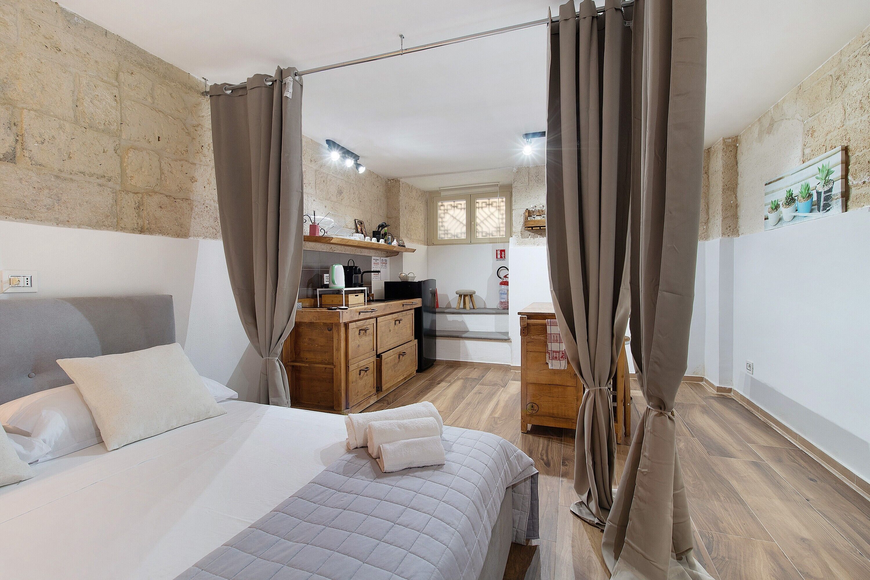 Une chambre comprenant un lit, des rideaux, une commode en bois, une kitchenette et une petite salle de bain.