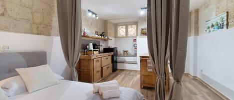 A bedroom with a bed, curtains, a wooden dresser, a kitchenette, and a small bathroom.