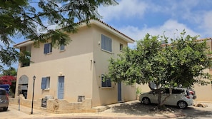 A two-story building with a beige facade, blue shutters, and a tree in front. - Villa Nadezda – 3-Bedroom Villa with Pool near Paphos Harbour (Pafos)