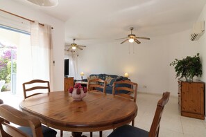 A dining area with a wooden table, chairs, ceiling fans, and a view of a balcony with a plant. - Villa Nadezda – 3-Bedroom Villa with Pool near Paphos Harbour (Pafos)