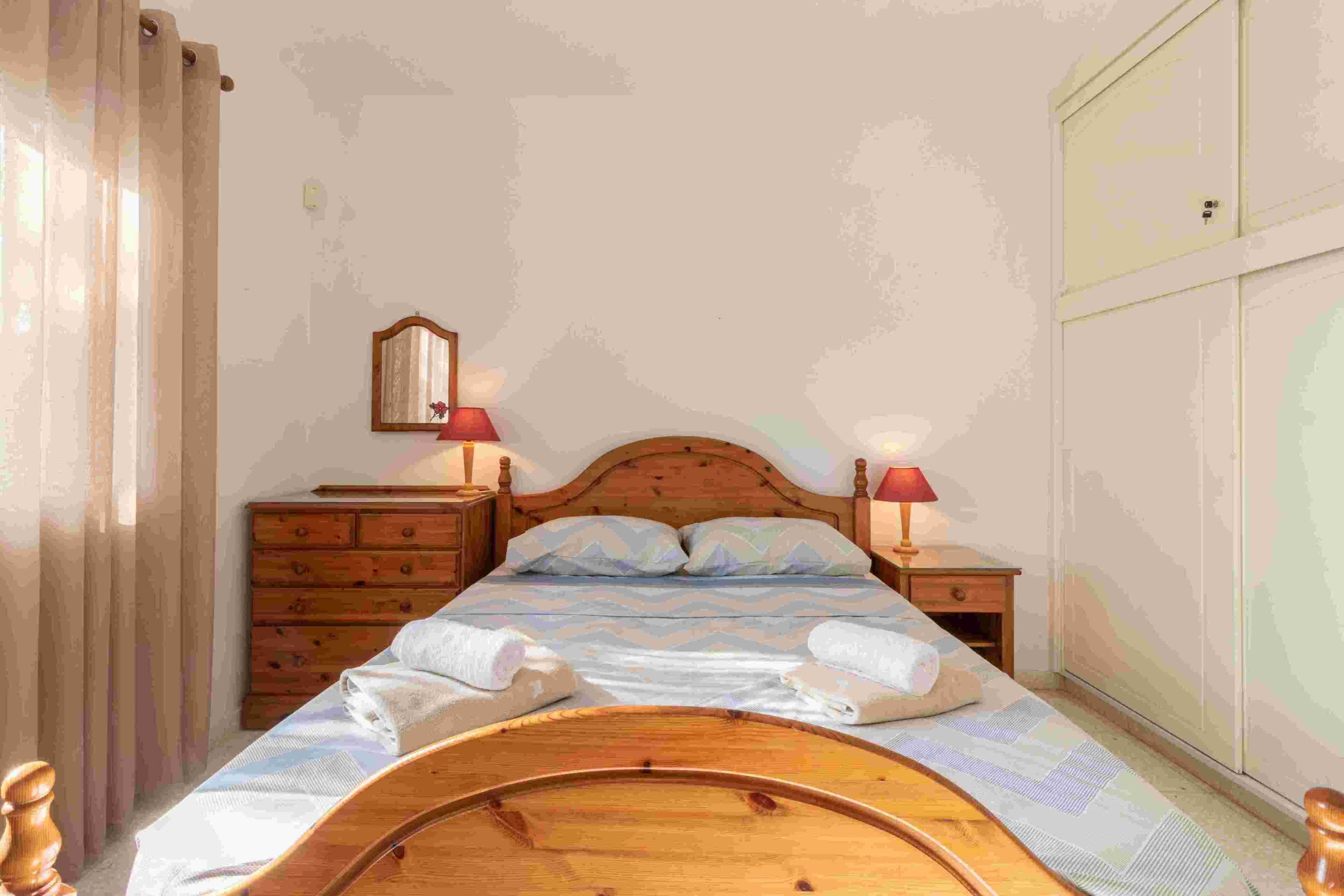 A bedroom with a wooden bed, two bedside tables with lamps, a dresser, and a wardrobe.
