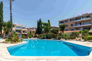 A swimming pool surrounded by palm trees and a multi-story building with balconies. - Villa Nadezda – 3-Bedroom Villa with Pool near Paphos Harbour (Pafos)