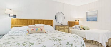 A bedroom with a large bed, two smaller beds, a ceiling fan, a round mirror, and a painting on the wall.