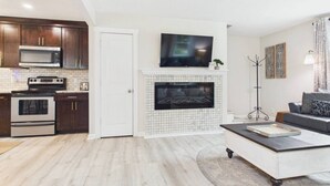 A modern living room with a fireplace, a flat-screen TV, and a sofa. - `The Harlow`- The Cottage Collection (Virginia Beach)