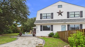 A two-story building with a star-shaped window, a paved driveway, and a wooden fence. - `The Harlow`- The Cottage Collection (Virginia Beach)