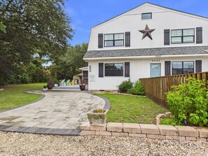 A two-story building with a star-shaped window, a paved driveway, and a wooden fence. - `The Harlow`- The Cottage Collection (Virginia Beach)