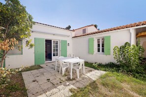 Um edifício branco com persianas verdes, uma mesa branca com cadeiras e um pátio de cascalho.