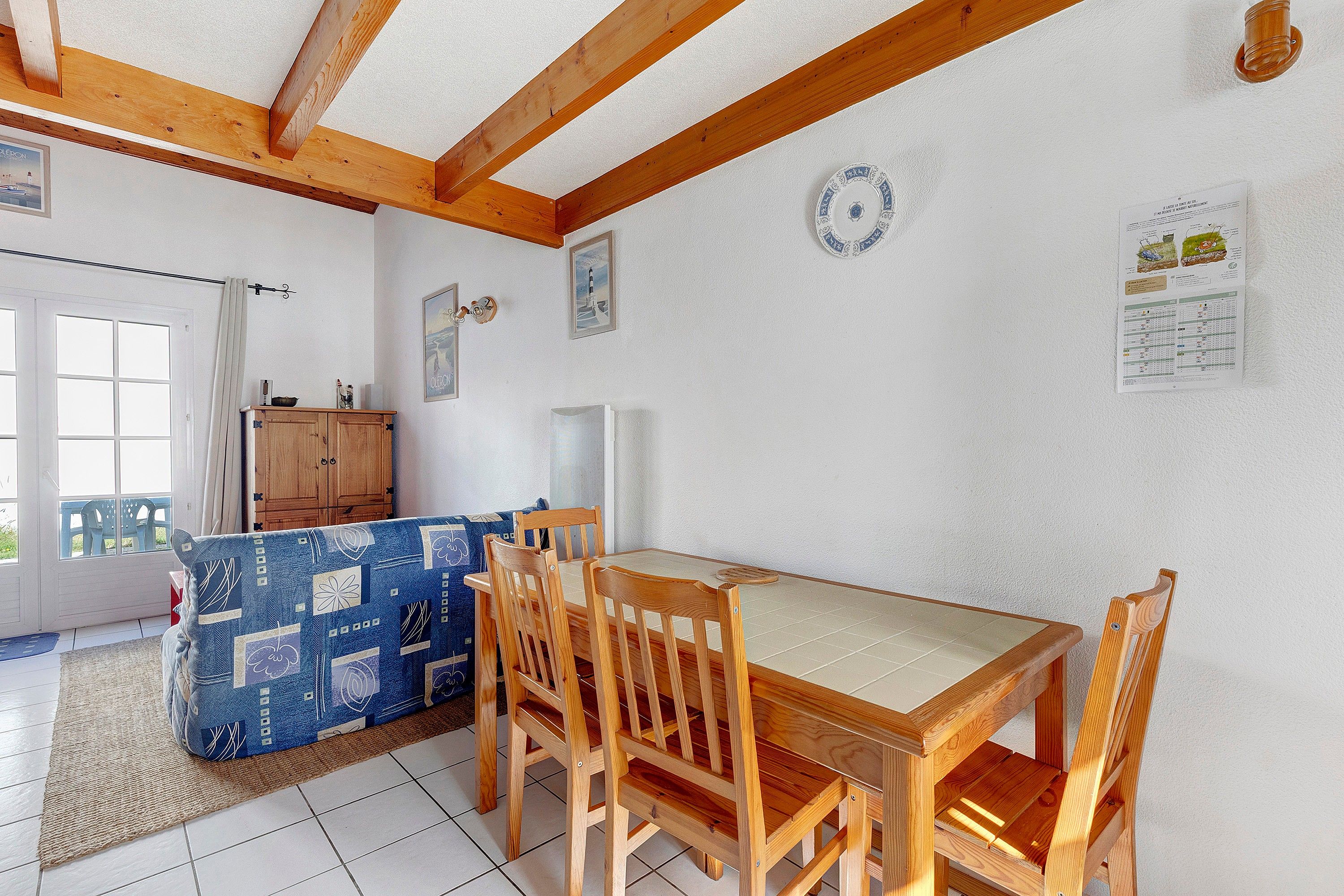 Uma sala de jantar com mesa e cadeiras de madeira, um sofá azul estampado e um armário.