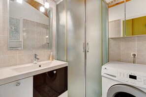 Casa de banho com lavatório, espelho e máquina de lavar roupa.