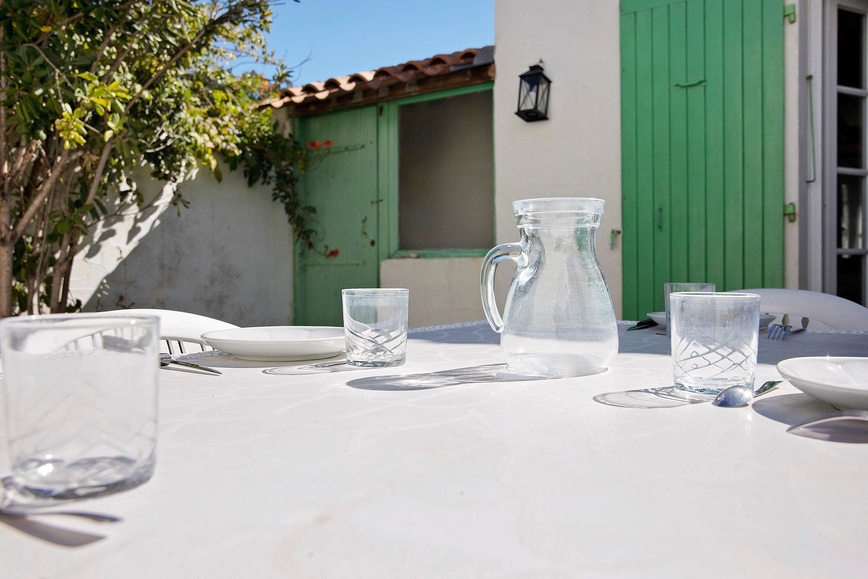 Une table dressée avec de la vaisselle transparente, une carafe et des assiettes, avec une porte verte et un mur blanc en arrière-plan.