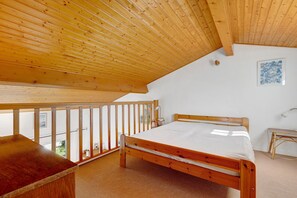 Quarto com teto de madeira, uma cama, uma escrivaninha e vista para o exterior.