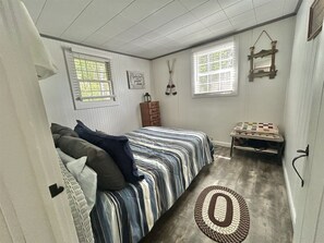 Ein Schlafzimmer mit einem Bett, einem Schminktisch, einem Fenster mit Jalousien und einem an der Wand befestigten Regal.
