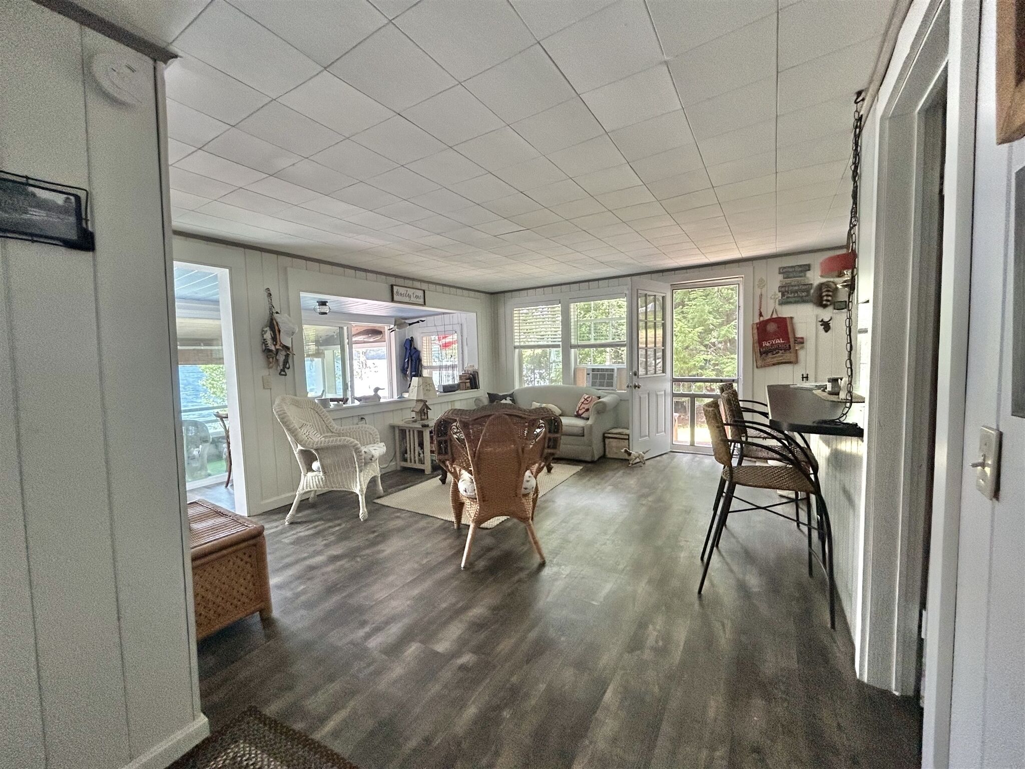 A spacious room with a large window, a white chair, a wicker chair, and a dining table.