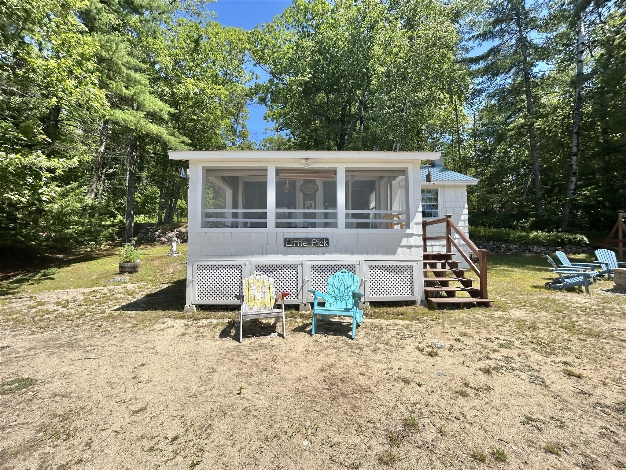 A cabin with a covered porch, a set of Adirondack chairs, and a staircase leading to an upper level.