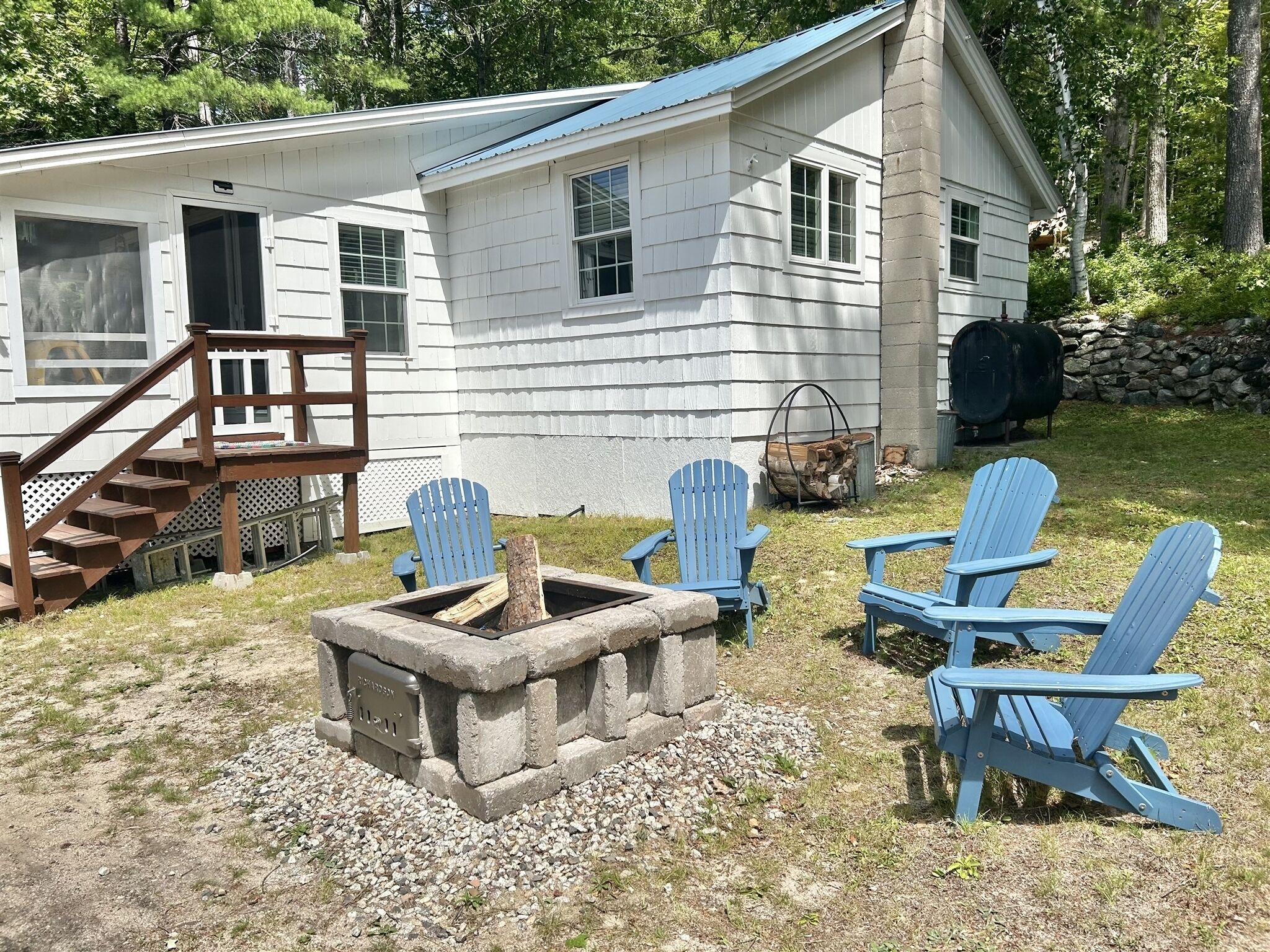 Une cabane dotée d’un foyer en pierre, d’une terrasse en bois et de fauteuils Adirondack.