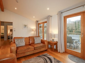 A spacious living room with a leather sofa, a small table with a lamp, and a view of an outdoor deck.