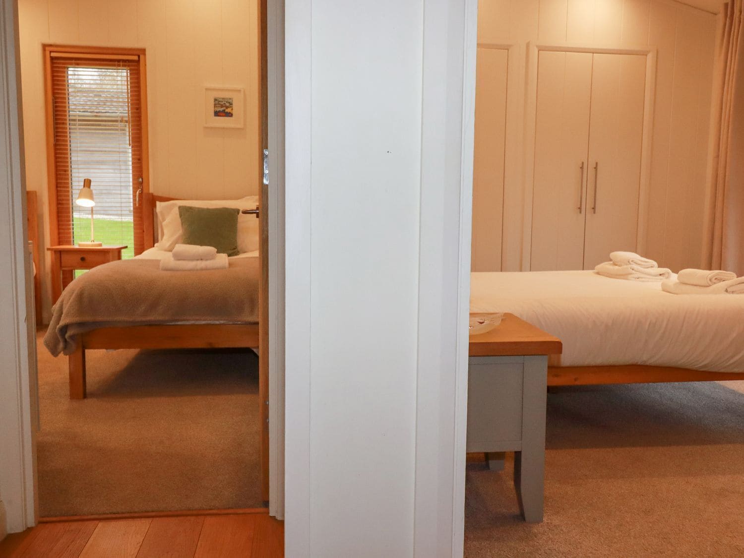 Quarto com duas camas, mesa de cabeceira, persianas e porta.