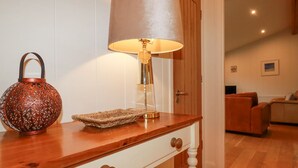 Una consola de madera con una lámpara, una cesta tejida y un recipiente decorativo de metal.