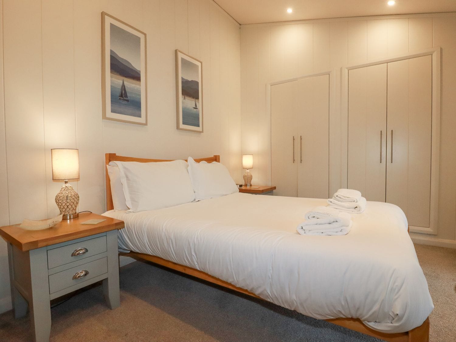 Een slaapkamer met een bed, twee nachtkastjes, een kledingkast en twee wanddecoraties.