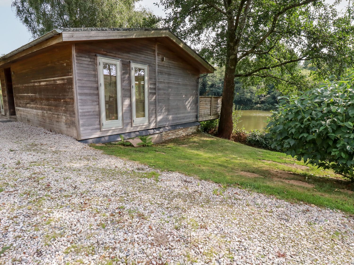 A wooden cabin with a gravel driveway and a grassy area.