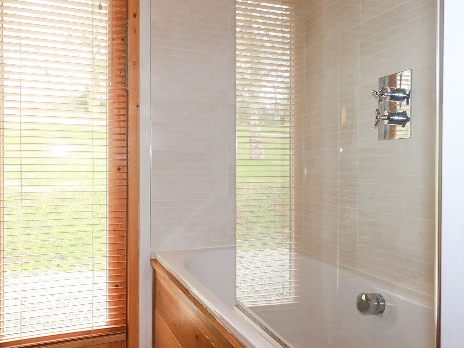 Une salle de bain avec une baignoire, des cadres de fenêtre en bois et un espace douche doté d’un robinet chromé.