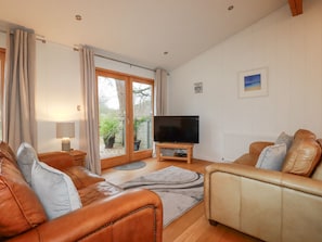 A living room with leather sofas, a television, and a view through a glass door to an outdoor area.