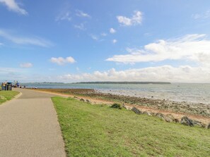 A coastal path with a paved walkway, grassy areas, and a view of the sea. - Glass House (Blandford Forum)