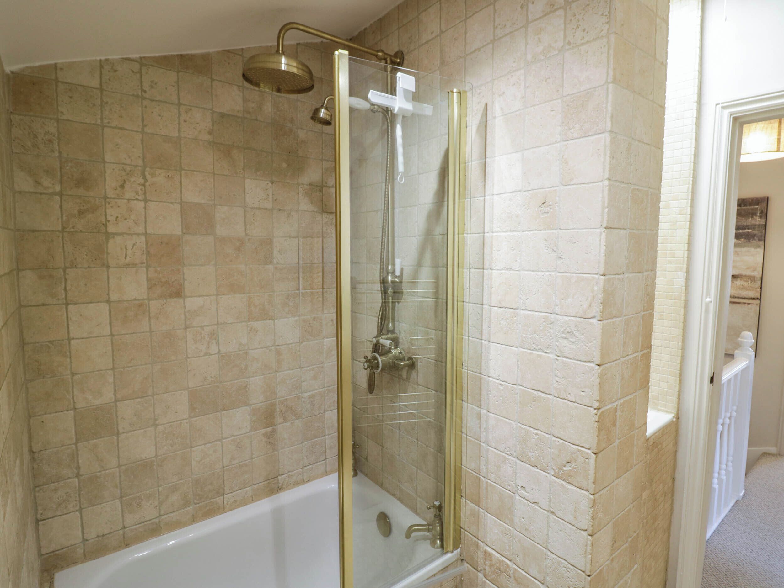 Ein Badezimmer mit einer gläsernen Duschkabine, einer weißen Badewanne und beige gefliesten Wänden.