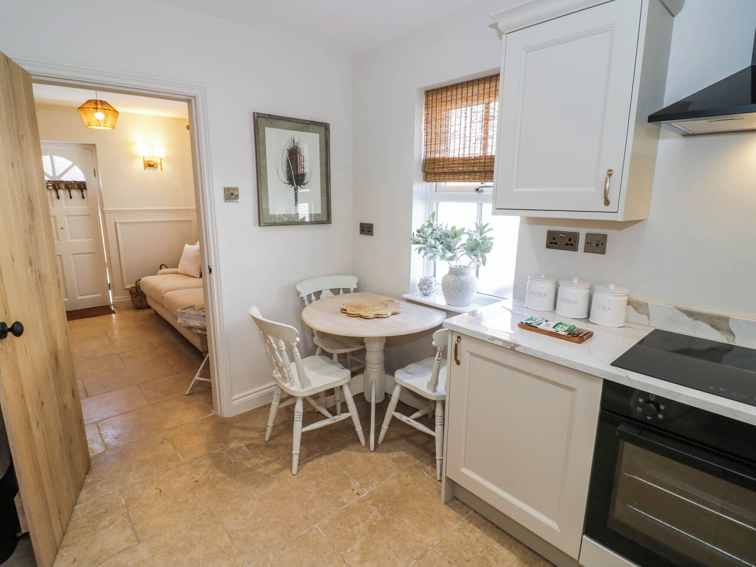 A kitchen with a dining table, chairs, a stove, and a window with a plant.