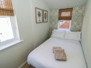 Ein Schlafzimmer mit einem Bett, zwei gerahmten Bildern, einem Fenster mit Blick und einer Wand mit Muster.
