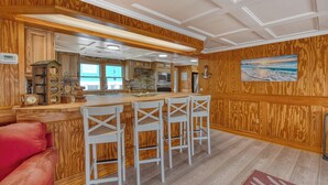 A kitchen with wooden paneling, a bar area with white chairs, and a red couch. - Luna May - Charming 2 Bedroom, 3 Bath Beach House (Garden City Beach)