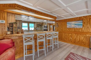 Eine Küche mit Holzvertäfelung, einer Bar mit weißen Stühlen und einem roten Sofa.