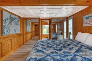 Ein Schlafzimmer mit einem großen Bett, Holzwandverkleidung, einem Gemälde an der Wand und Blick durch eine offene Tür.
