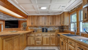 A kitchen with wooden cabinets, a stone backsplash, and a built-in dishwasher. - Luna May - Charming 2 Bedroom, 3 Bath Beach House (Garden City Beach)