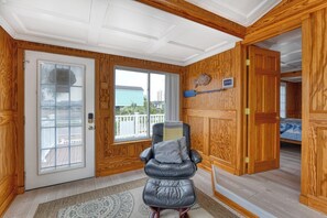 Ein Zimmer mit einer Glasschiebetür, die auf einen Balkon führt, einem Ledersessel und einem Bett mit blauer Steudecke.