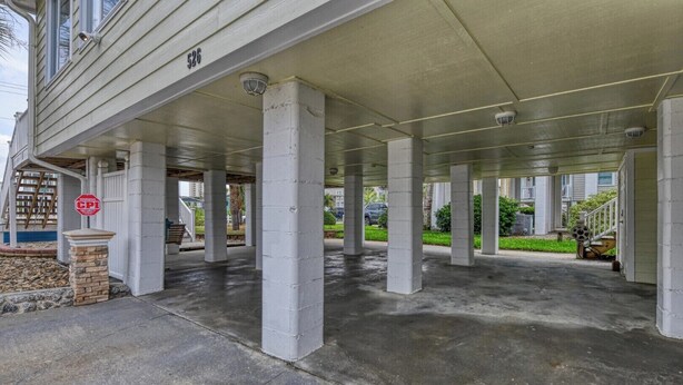 A covered parking area with concrete pillars, a security warning sign, and a building entrance. - Luna May - Charming 2 Bedroom, 3 Bath Beach House (Garden City Beach)